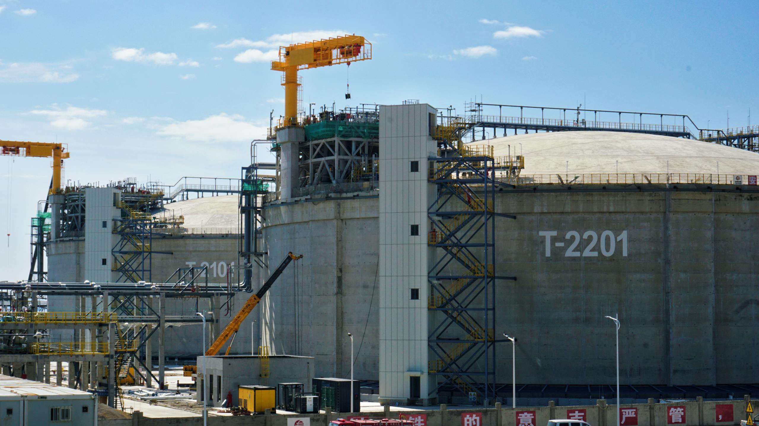 Large industrial storage tanks with cranes in a sunny facility setting.